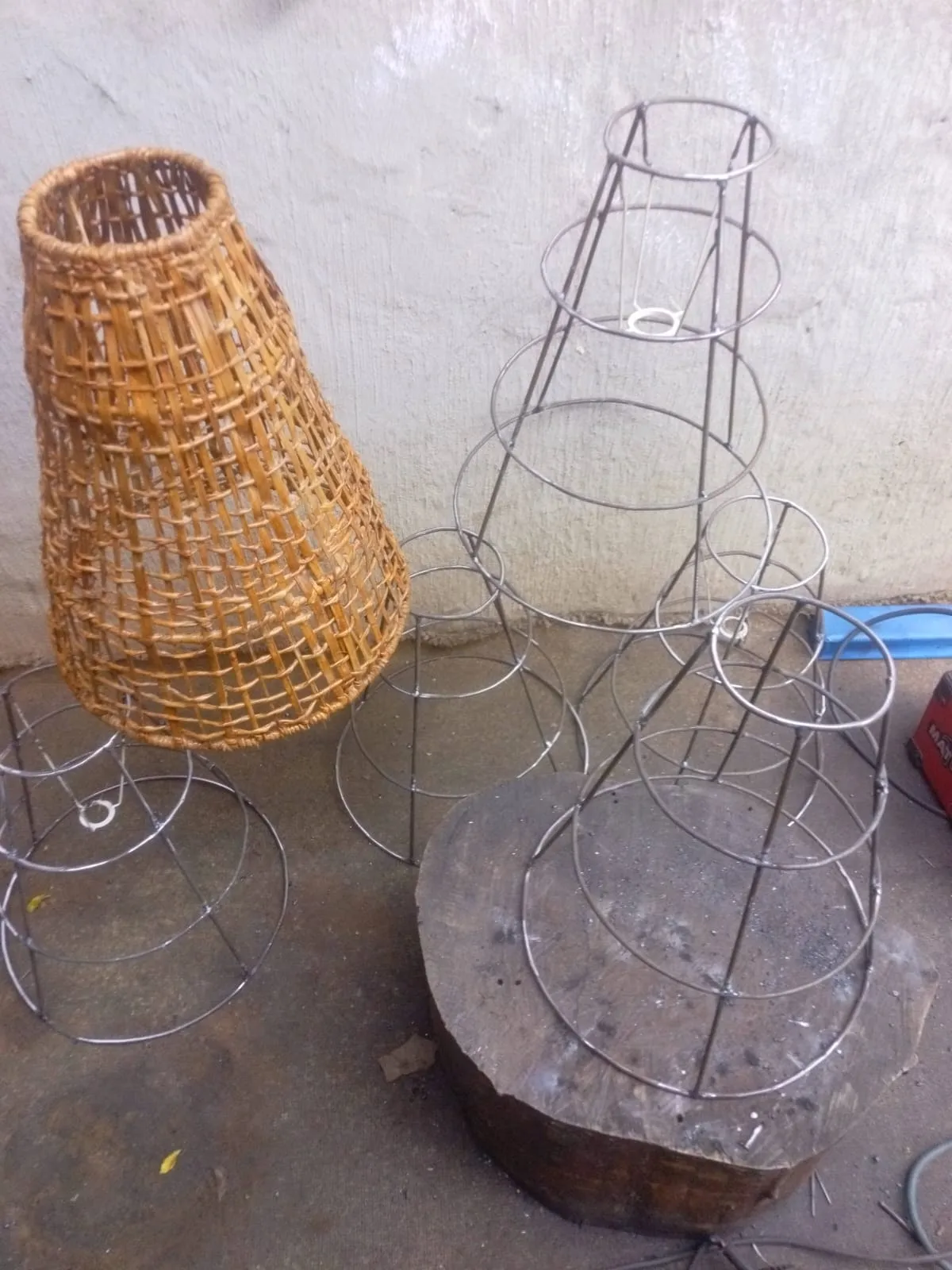 Set of hand-made wire lampshade frames beside the original woven rattan shade they were copied from