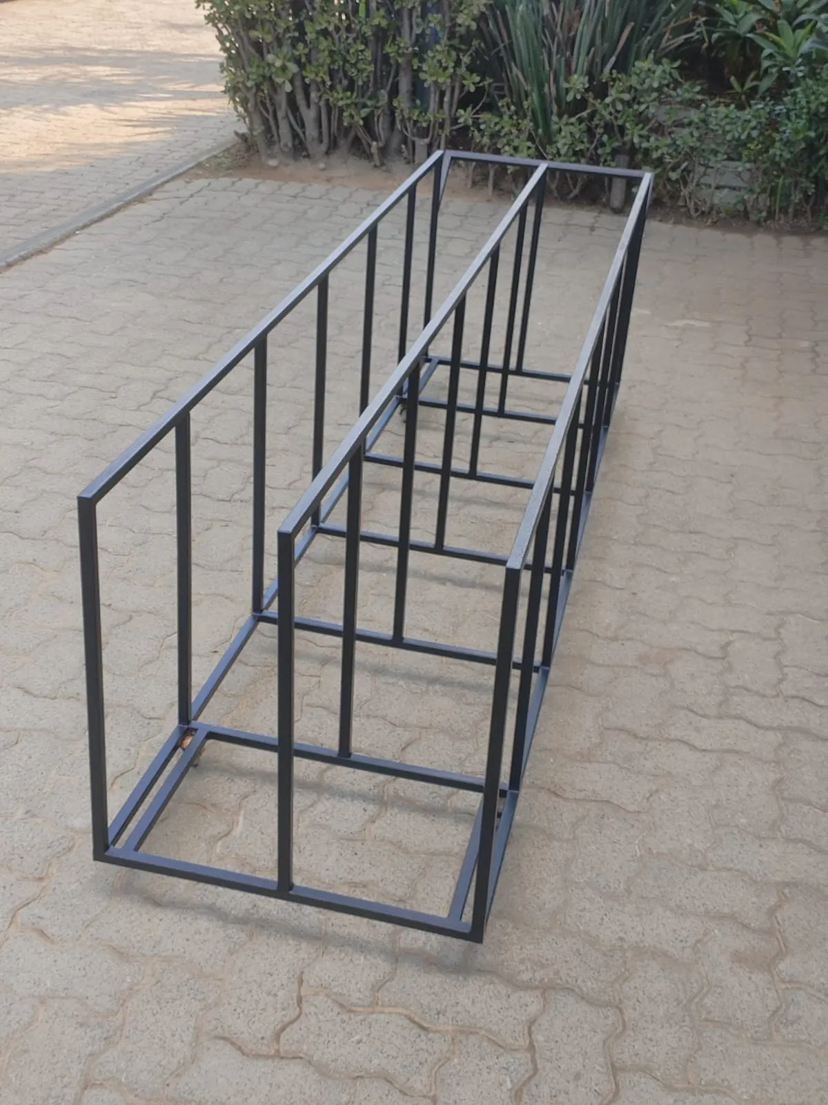 Tall double-sided black steel storage rack with vertical dividers, standing on a paved driveway