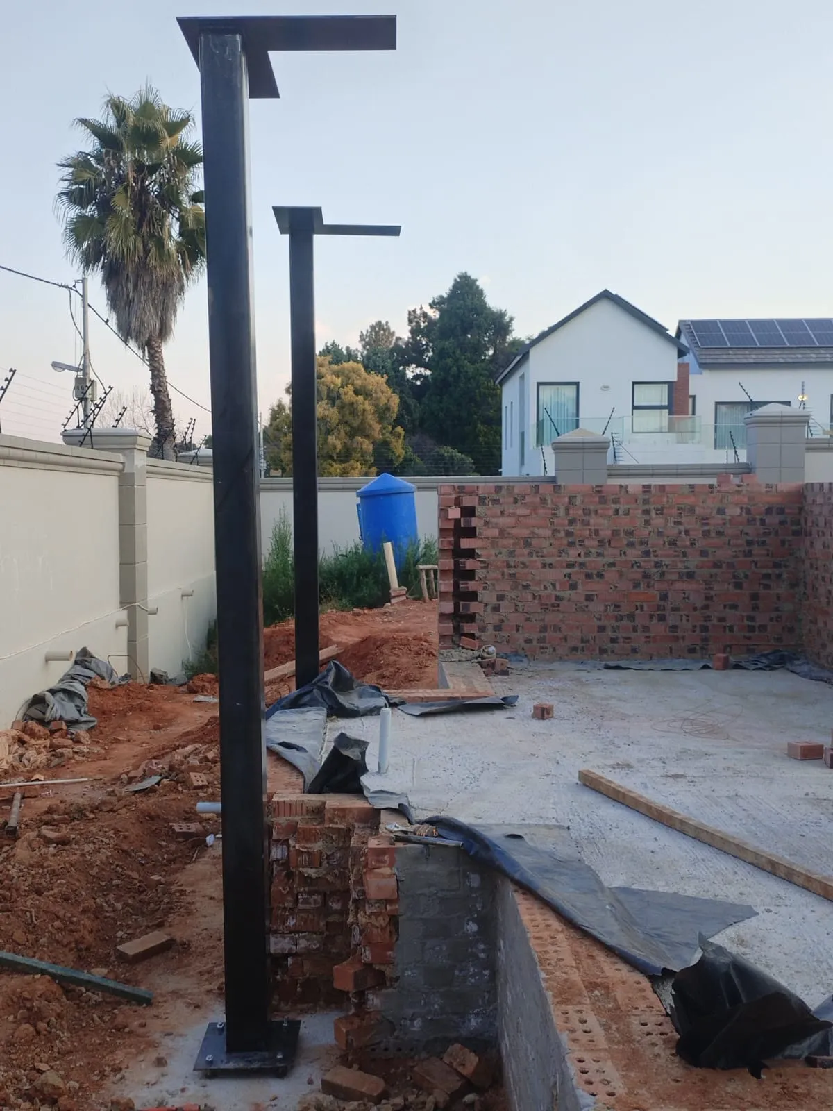 Two black structural steel columns with welded head plates standing on a residential building site