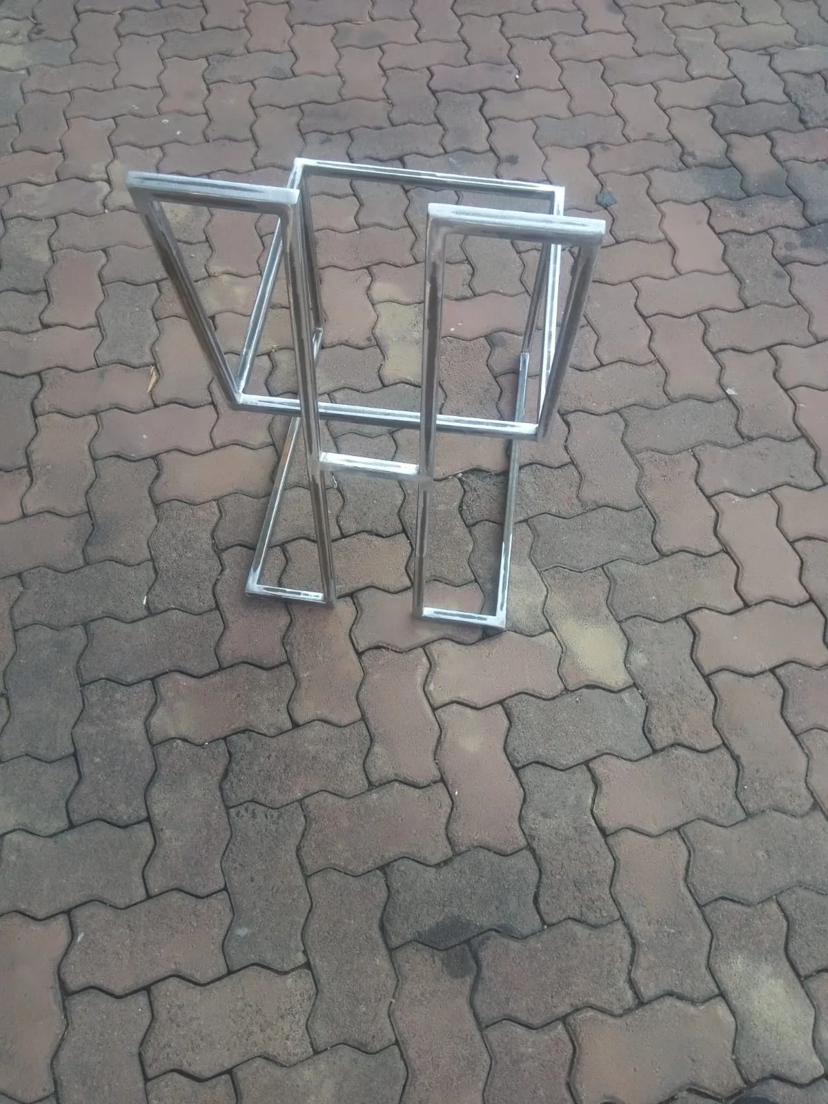 Polished stainless steel table base with angled legs and a square top frame, on paving